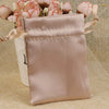 A light pink satin drawstring pouch with a beige ribbon and floral accents.