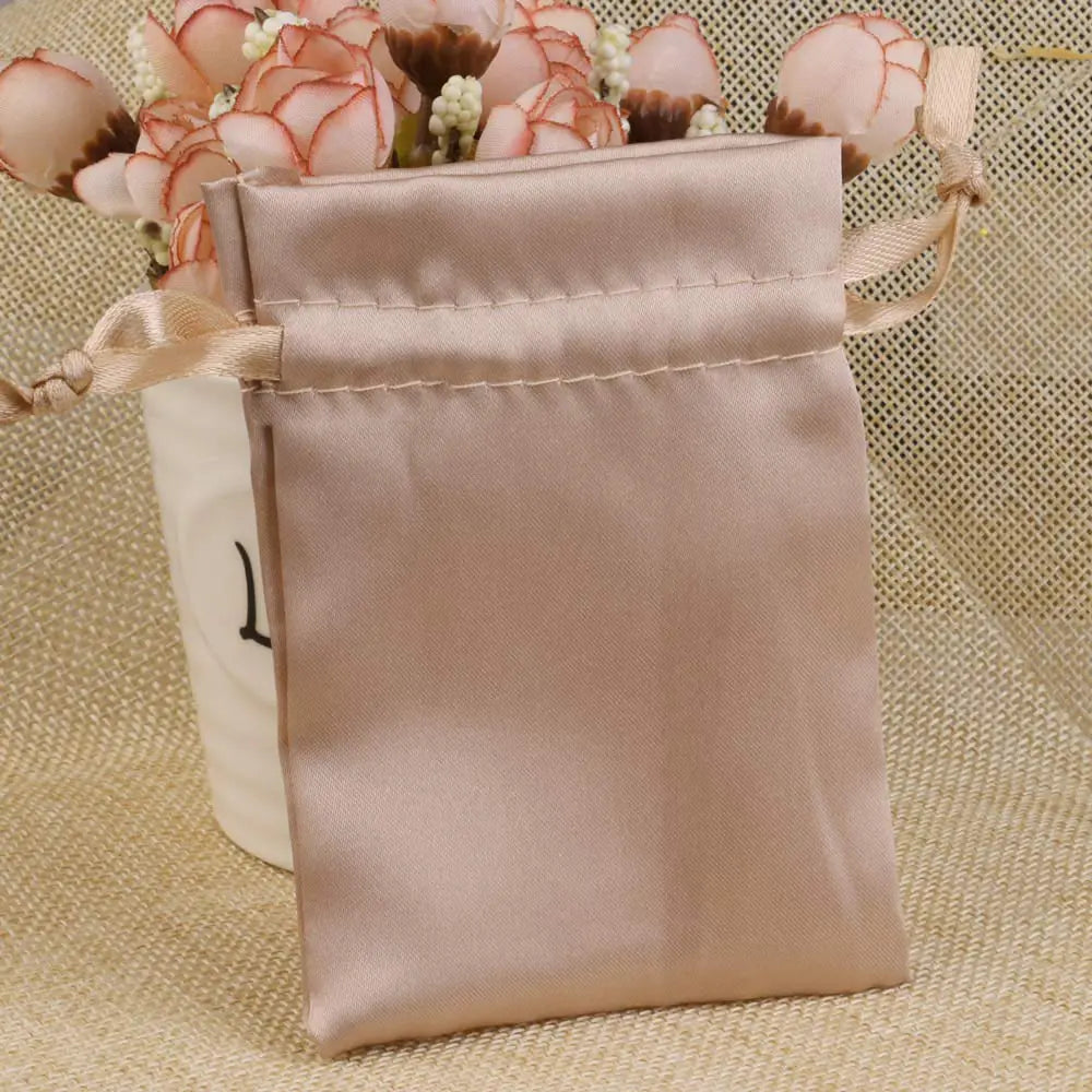 A light pink satin drawstring pouch with a beige ribbon and floral accents.