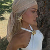 A woman wearing a beige bohemian lace trim shawl draped over her hair, posing outdoors against a tree.