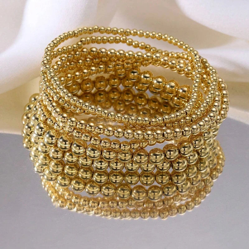 A stack of gold-colored minimalist round beaded bracelets for women