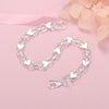 A silver heart charm bracelet made of sterling silver links and charms is displayed on a pink background.