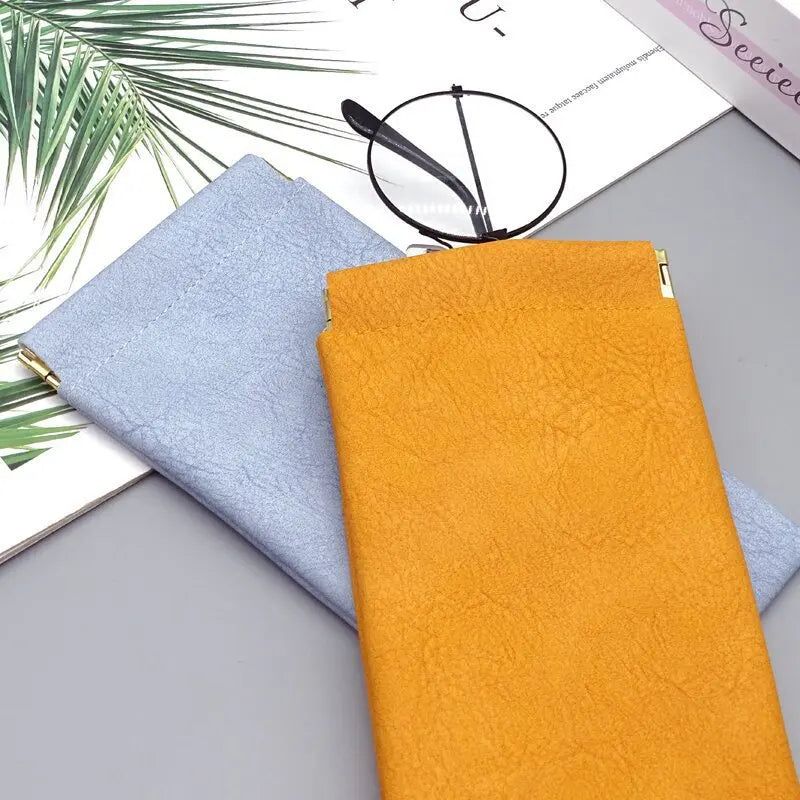 A bright orange premium PU leather eyewear storage bag next to a light blue one on a gray surface.