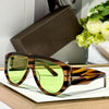 Brown tinted oversized pilot sunglasses resting on a white surface next to a dark box and green flowers.
