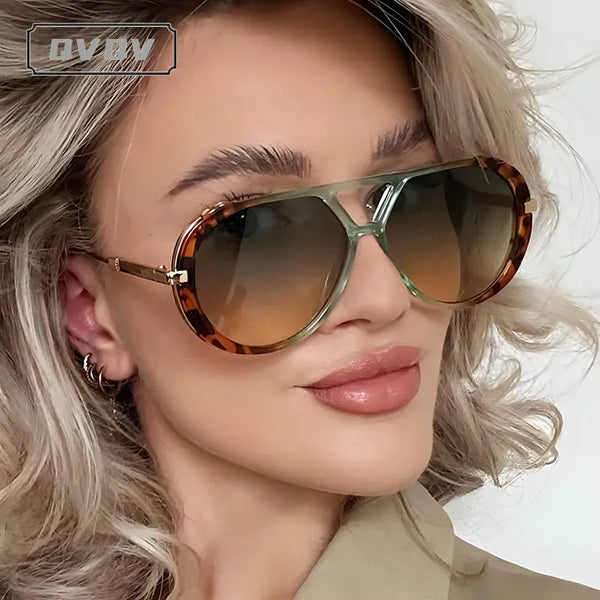 امرأة تعرض نظارات شمسية عصرية بتدرج لوني كبير مع شعر أشقر فاتح وسترة بيج.