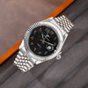 A silver-toned men's wristwatch with a black dial and a metal bracelet is shown on a gray background.