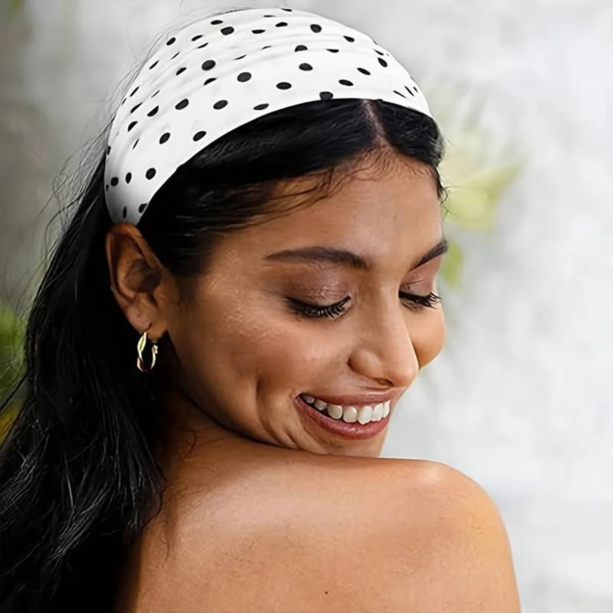 A woman wearing a black and white polka dot stretch headband on her dark hair.
