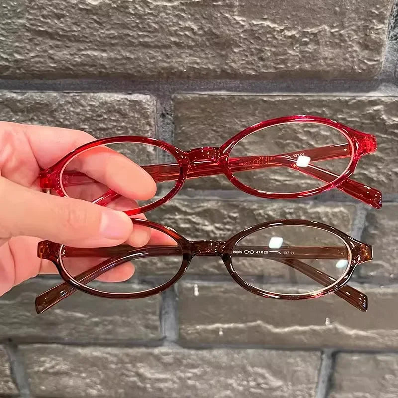 Une main tient des lunettes de mode ovales rétro teintées en rouge sur un fond de briques grises.