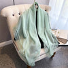 A light mint green shawl with delicate lace trim draped over a cream upholstered chair.