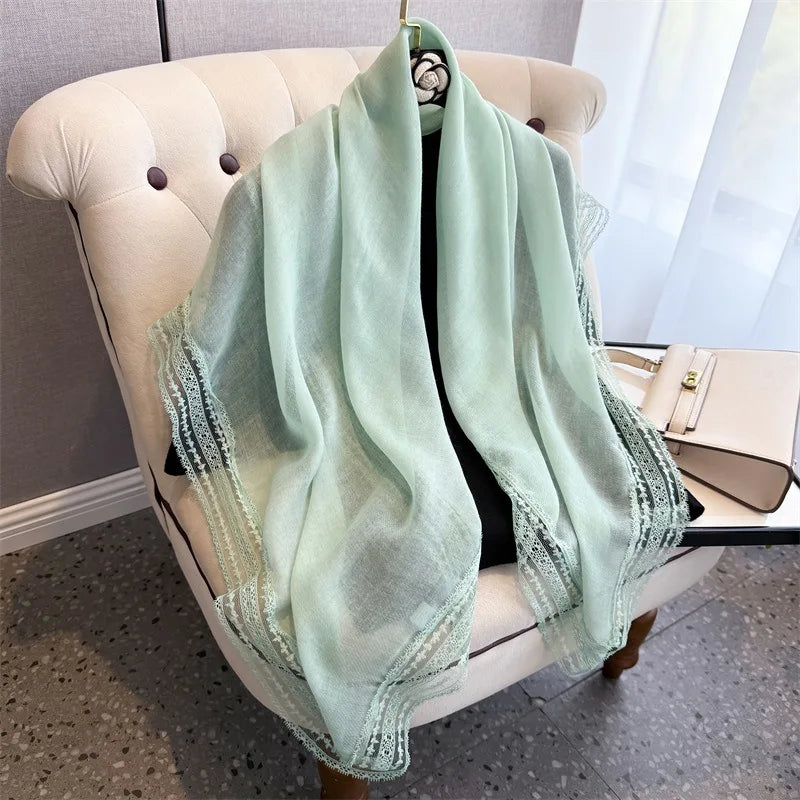 A light mint green shawl with delicate lace trim draped over a cream upholstered chair.