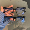 A person holds a pair of black-framed, blue-tinted anti-blue light spectacles against a gray background.
