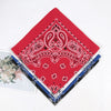 A red bandana scarf featuring white paisley embroidery and detailing, laid diagonally on a white background.