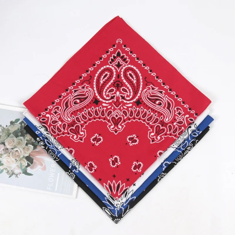 A red bandana scarf featuring white paisley embroidery and detailing, laid diagonally on a white background.