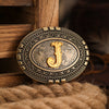 A vintage western belt buckle with an ornate gold design and dark metal finish resting on a woven surface.