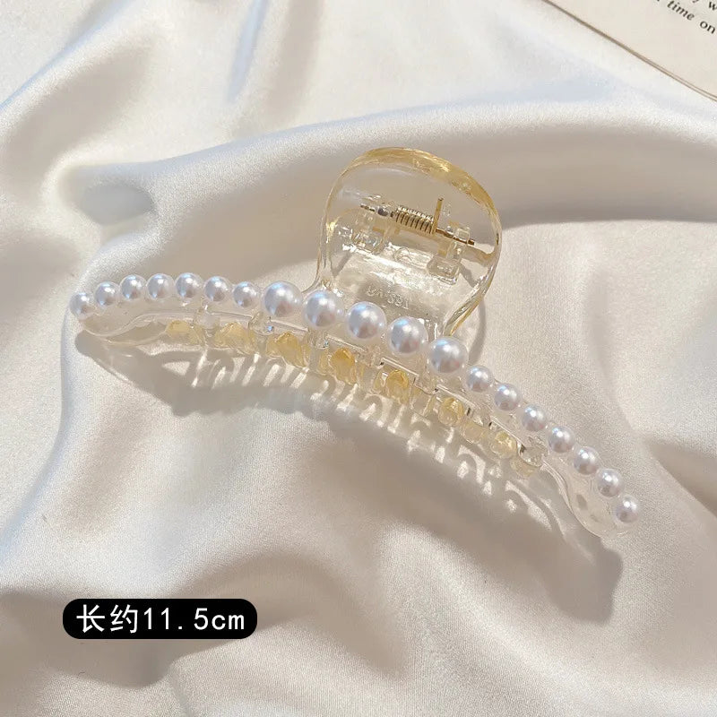 Clear acrylic hair claws adorned with small white simulated pearls displayed on a white satin fabric.