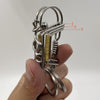 Un porte-clés mécanique en acier inoxydable avec une boucle et des ressorts enroulés est tenu dans une main.