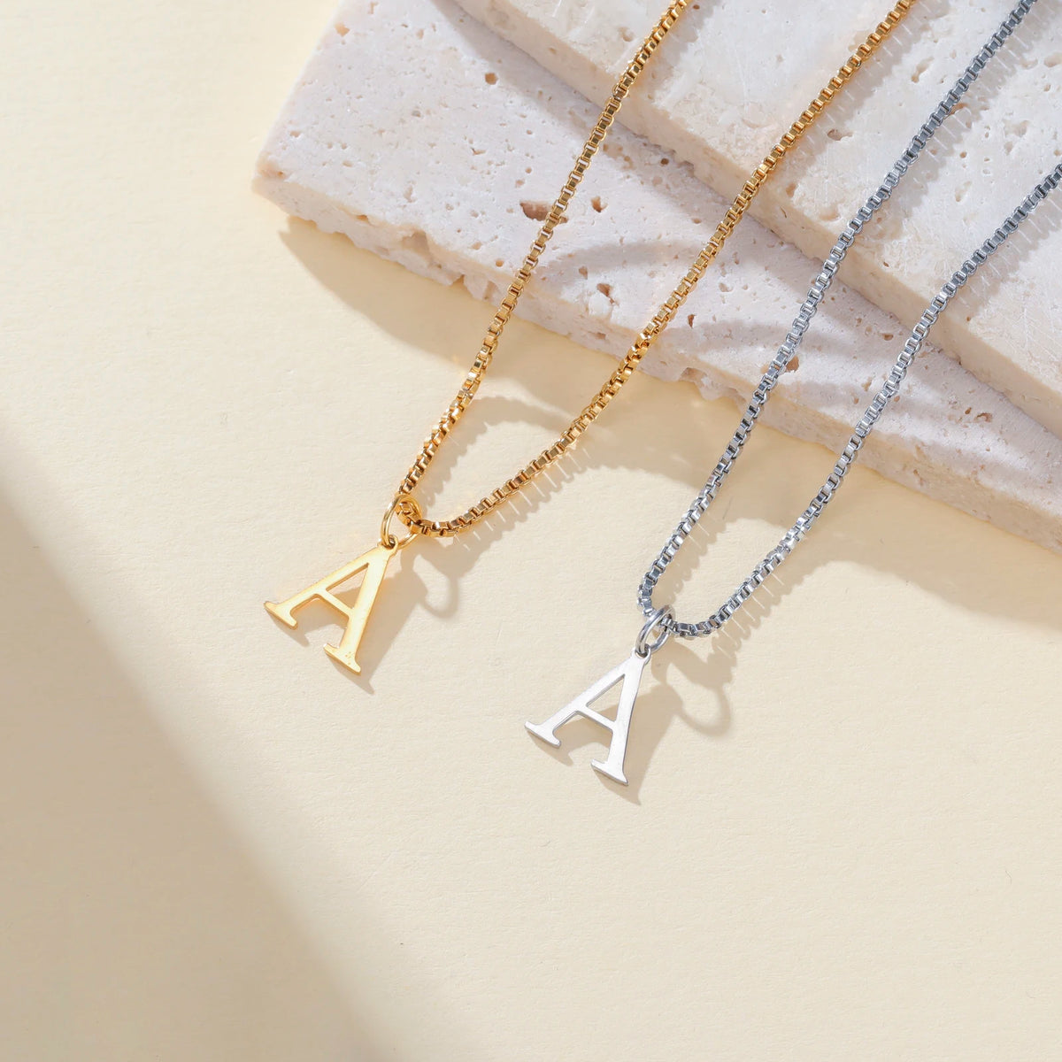 Two necklaces featuring initial letters A in gold and silver chains displayed on a light background.