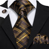 A close-up of a men's silk jacquard tie featuring a black and gold plaid pattern worn with a black suit jacket.