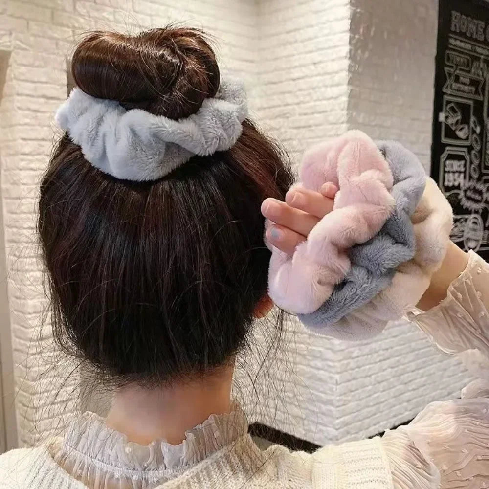 Une main tient des élastiques pour cheveux en tricot flou de couleur rose et gris sur un fond de cheveux foncé.