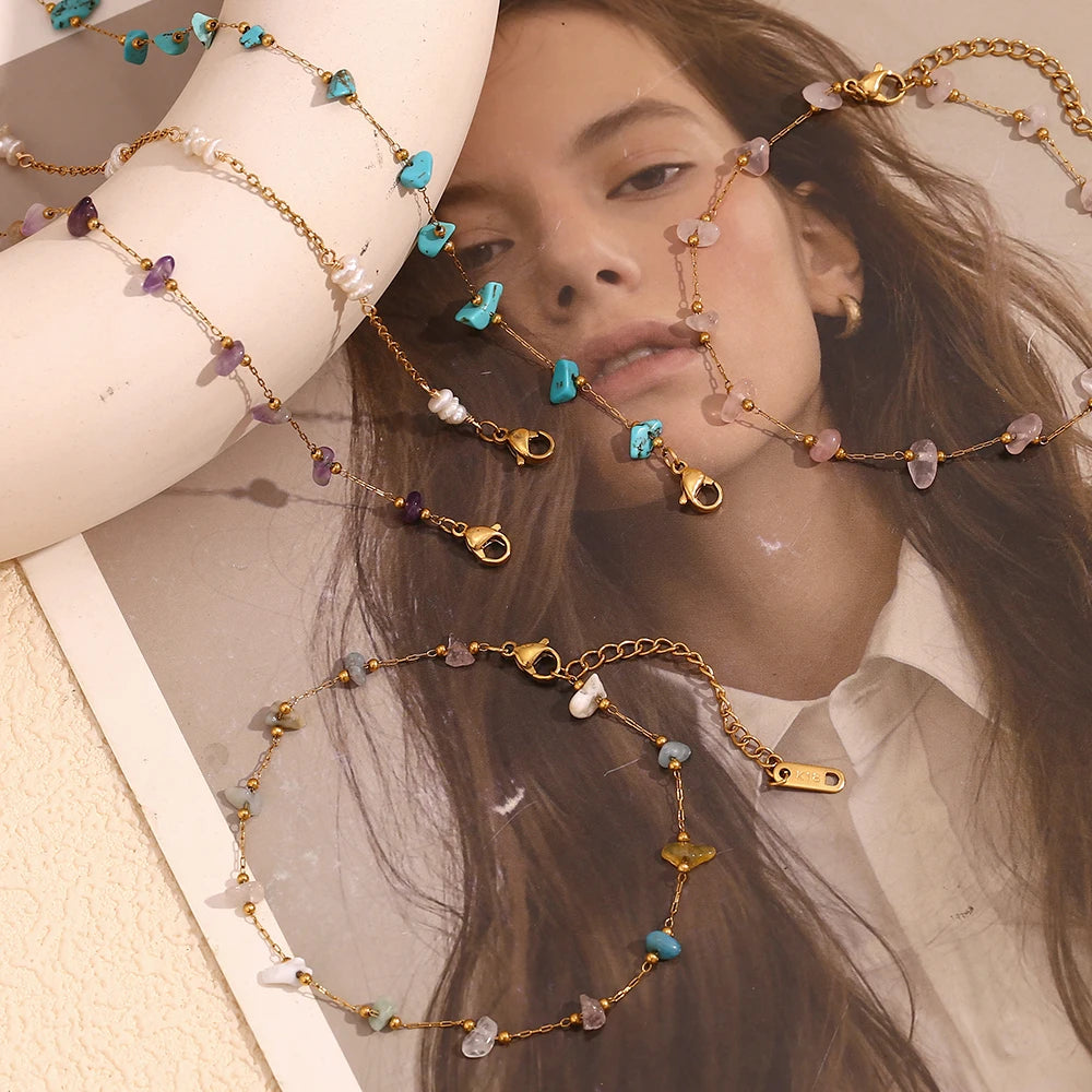 A model is wearing several delicate gold-plated foot chains adorned with small blue and purple crushed stones.