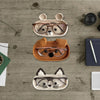 Three handmade crochet animal eyeglass storage cases in various colors and styles resting on a wooden surface.