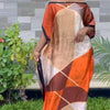 Eine Frau trägt ein orange-beigees, bohemissilbergedrucktes Kaftankleid im Freien.