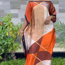 A woman wearing an orange and beige bohemian silk printed kaftan dress outdoors.