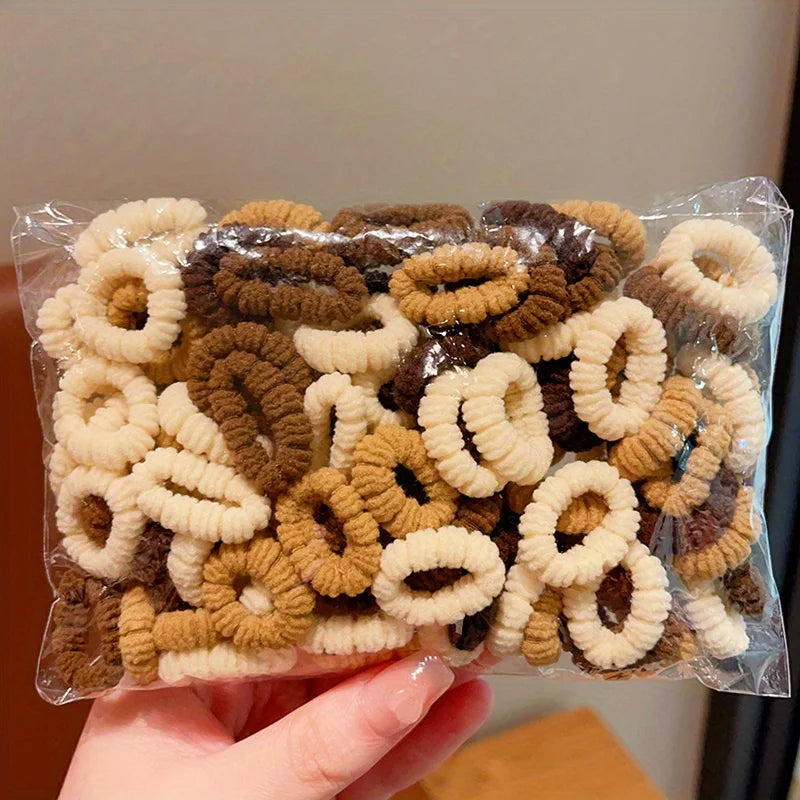 A pile of cute elastic hair bands in various shades of brown and beige is shown in a clear plastic bag.