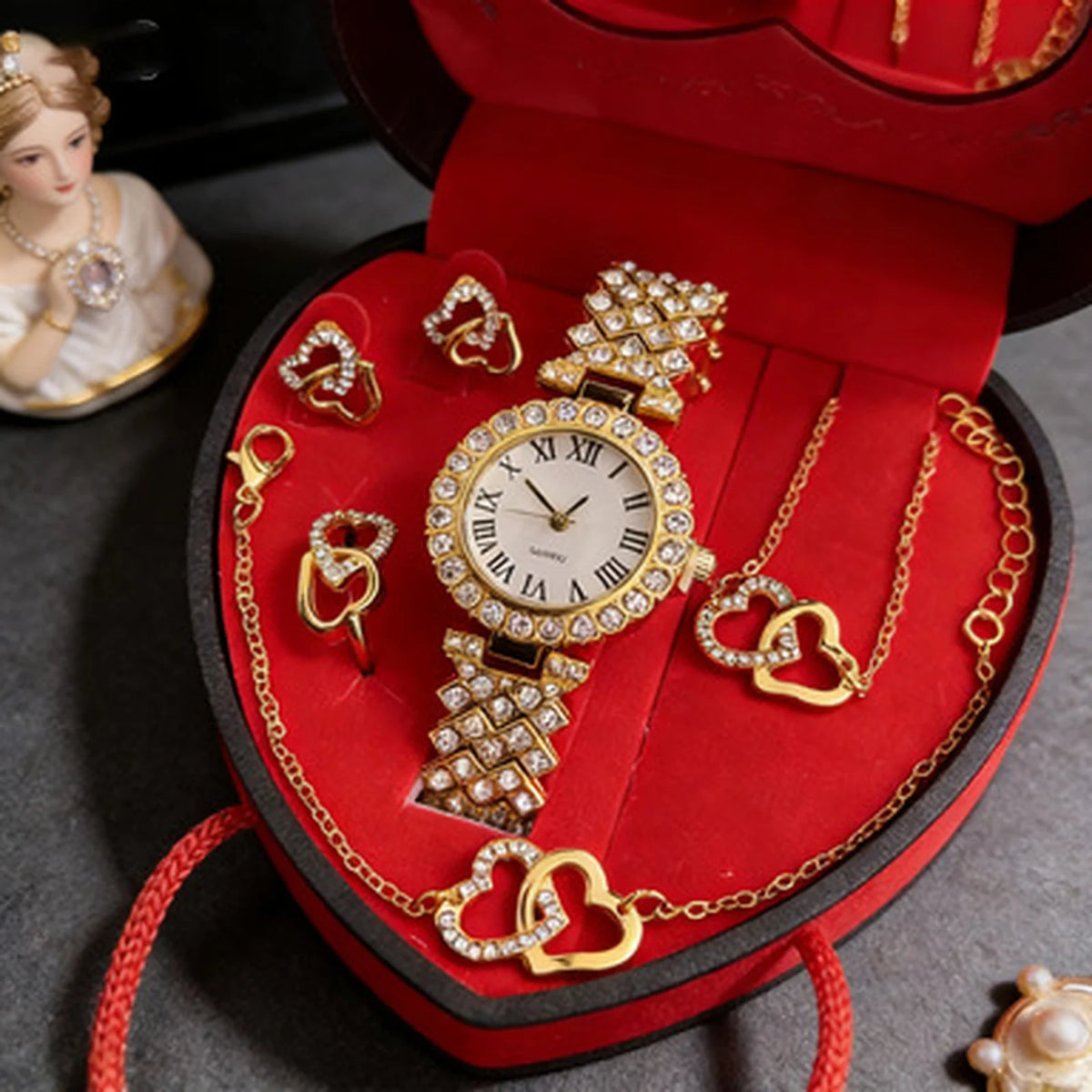 A red velvet jewelry box containing a gold-toned watch and several heart-shaped rhinestone necklaces.