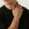 A close-up of a man wearing a personalized stainless steel cross Cuban chain bracelet on his wrist.
