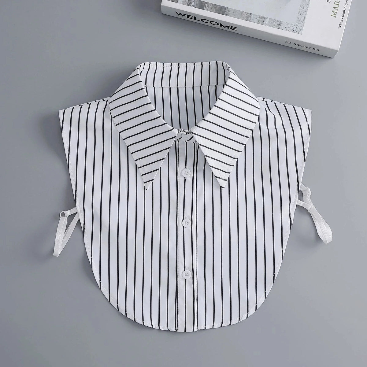 A white and black striped blouse with a false collar and detachable necklines displayed on a gray background.