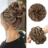 A close-up of a woman's hair styled in an elegant, textured updo with loose curls and a matching messy bun hair piece scrunch