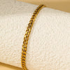 A gold-toned multi-chain stainless steel anklet is shown draped on a white fabric background.