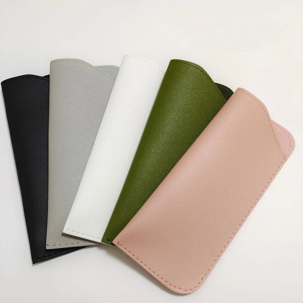 A row of five stylish PU leather glasses cases in shades of black, gray, white, olive green, and blush pink.