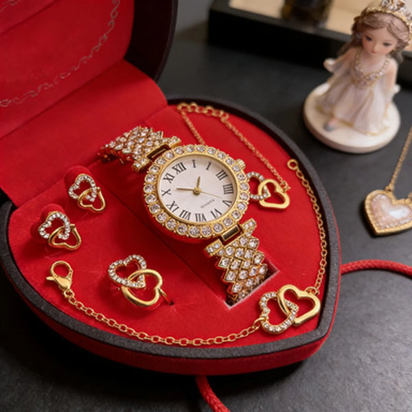 A red velvet jewelry box containing a gold-toned watch and various rhinestone heart-shaped necklaces and earrings.