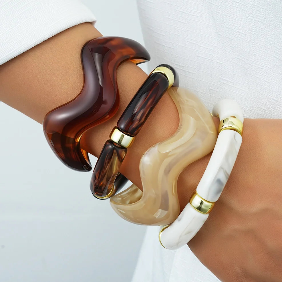 A set of vintage minimalist wavy bangle bracelets in dark amber and creamy white marble designs worn on a wrist.
