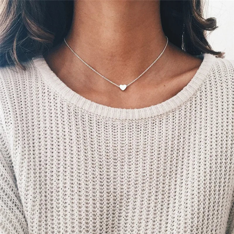Gros plan d'une femme portant un délicat collier de perles minimaliste argenté contre un pull clair.