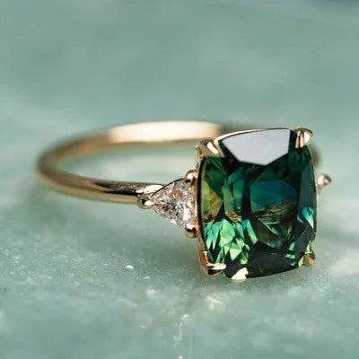 A vintage square gemstone four-claw ring featuring a deep green emerald cut stone set in gold.
