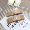 A beige elastic casual belt with a round silver buckle is displayed on a white card.