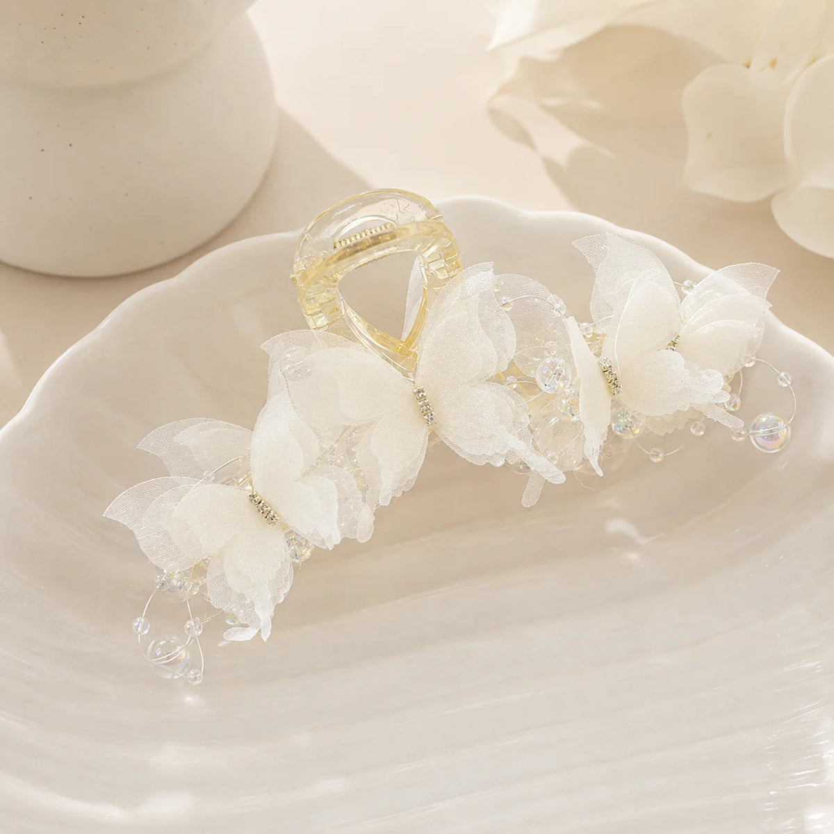 A gold pearl rhinestone butterfly hair claw clip resting on a white ceramic plate.