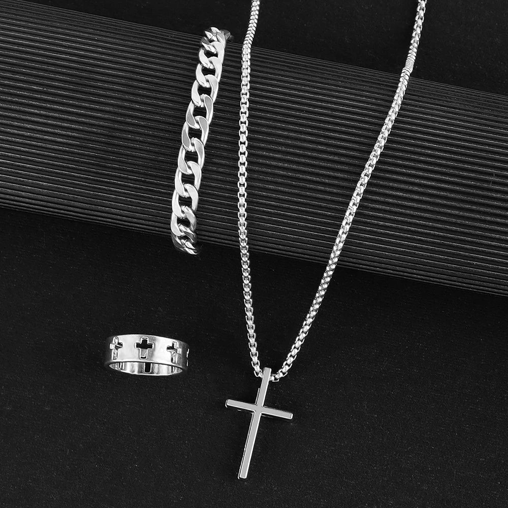 Collier en croix en acier inoxydable argenté et bracelet de chaîne argenté sur une surface sombre.