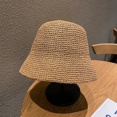 A hand-woven straw visor hat in a natural beige color resting on a wooden table.