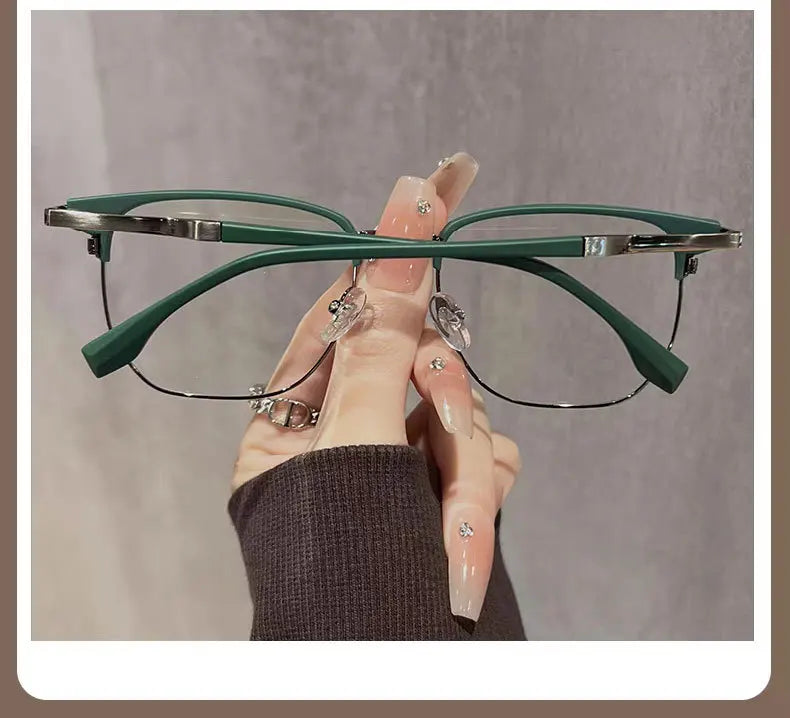 Eine Hand hält eine grüne Anti-Blau-Licht-Lesebrille mit silbernen Akzenten vor einem neutralen Hintergrund.