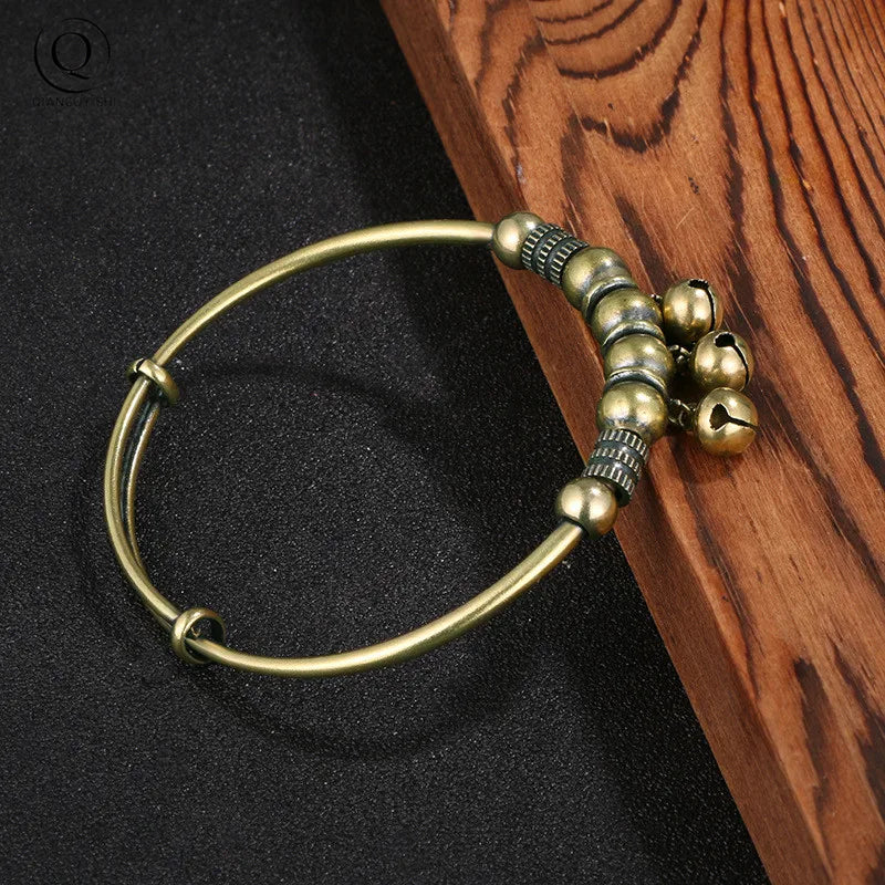 A vintage brass bell charm bracelet is displayed on a dark surface next to a wooden background.
