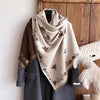 A beige pashmina shawl with a floral print is draped over a gray coat, displayed against a wooden background.