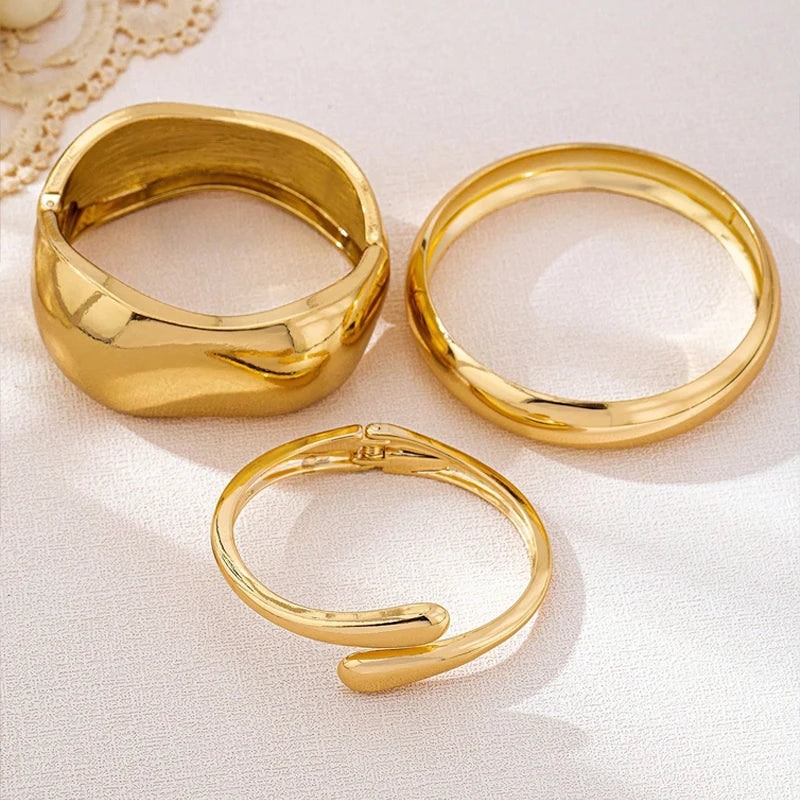 A set of three gold geometric wave bangle bracelets displayed on a white surface.