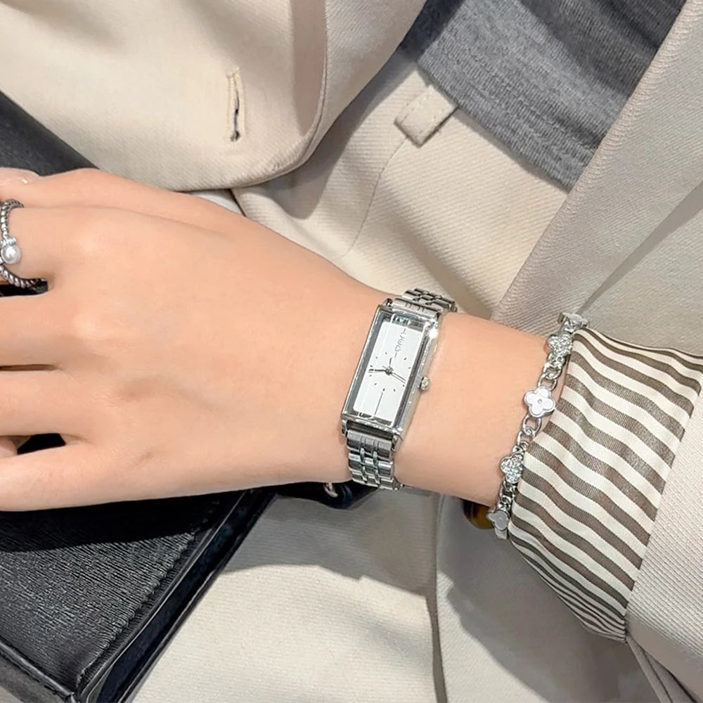 A close-up of a woman's wrist wearing a vintage gold stainless steel quartz watch and striped bracelet against a light blazer
