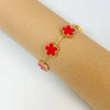 A gold plated stainless steel double-sided petal bracelet with red floral charms is displayed on a rolled beige fabric.