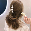 A woman's hair styled in a low ponytail with simulated pearl hair claws attached to the side.