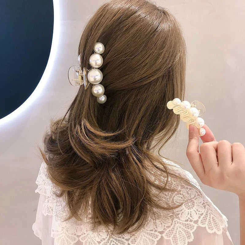A woman's hair styled in a low ponytail with simulated pearl hair claws attached to the side.