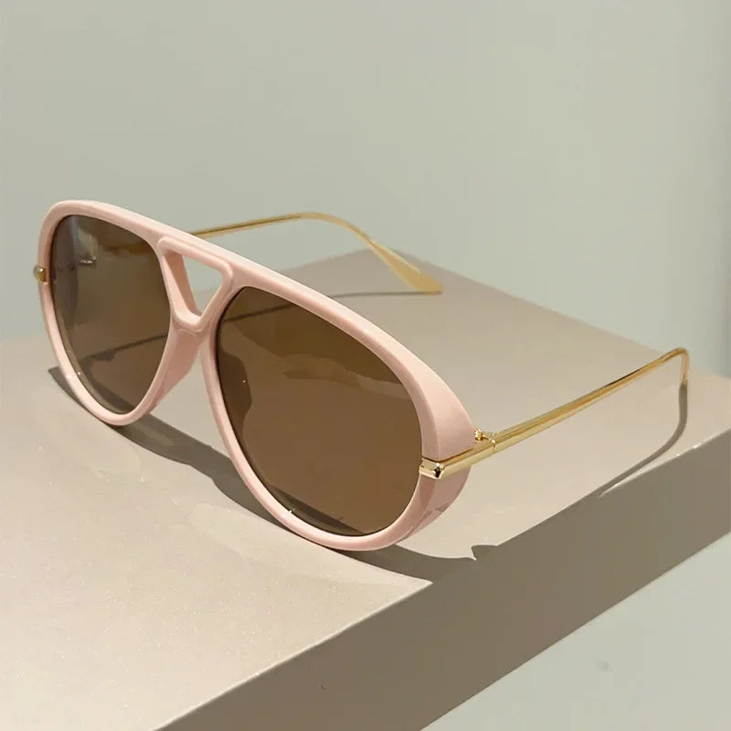 Pink aviator style sunglasses with gold-tone arms resting on a light surface.